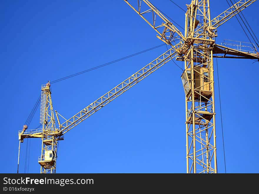 Two yellow cranes crossing on background with blue sky. Two yellow cranes crossing on background with blue sky