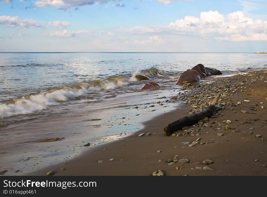 Pebbly abd sand sea coast, blue sky with clouds and water