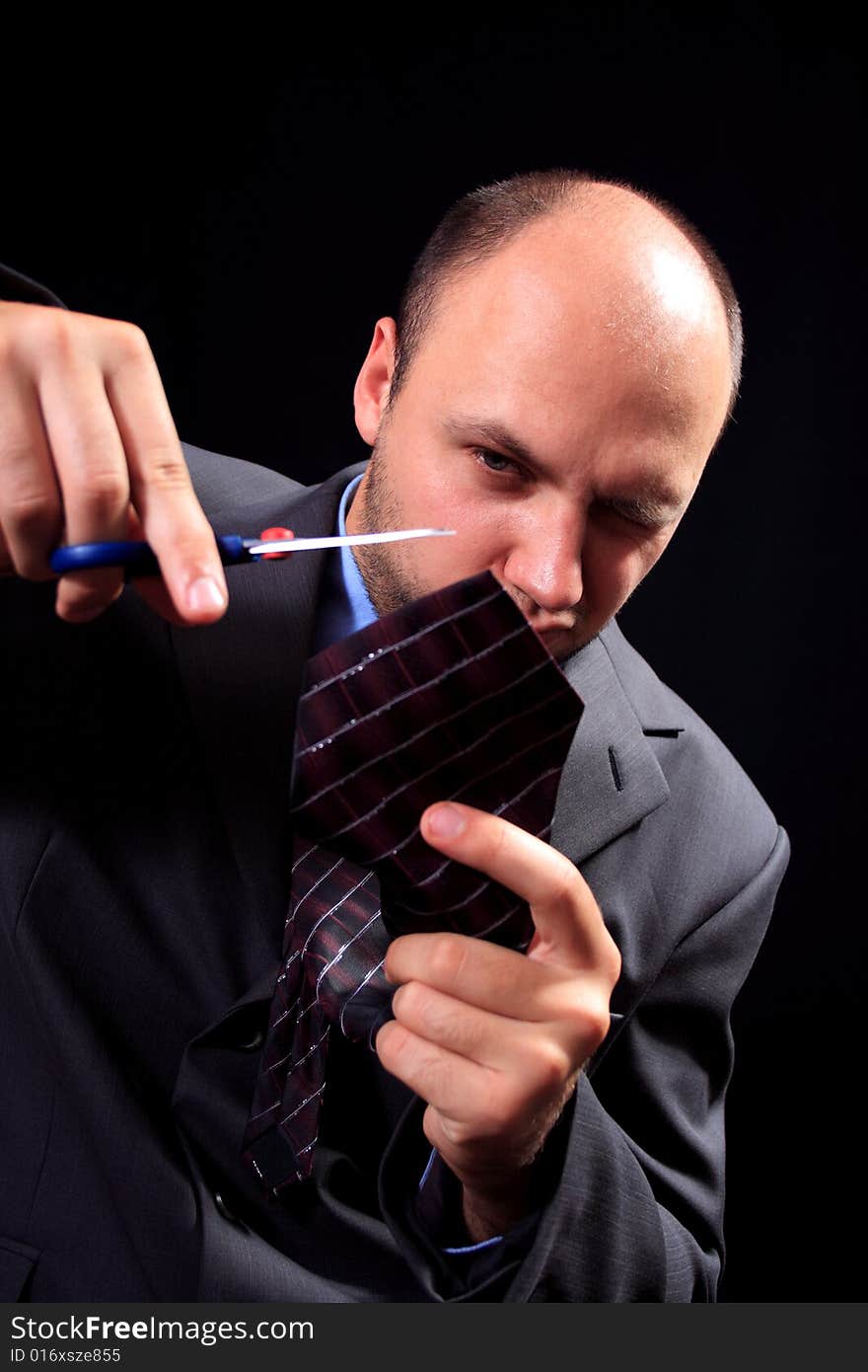 Man in a business suit scissors the tie, on a black background. Man in a business suit scissors the tie, on a black background