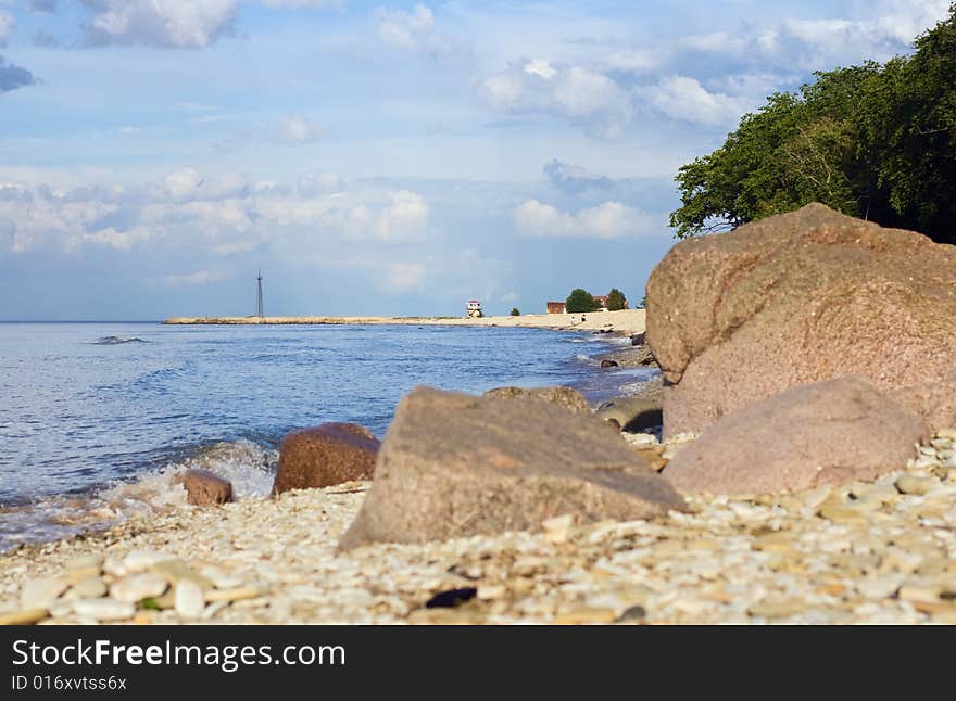 Pebbly sea coast, blue sky with clouds and water