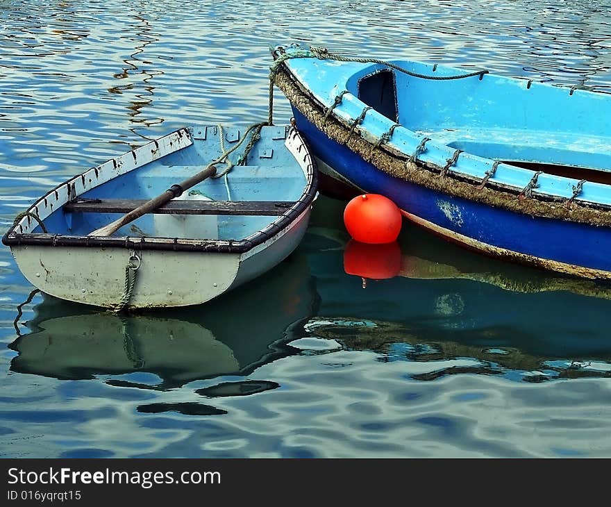 Two old skiffs with peeling paint tied-up in harbour.