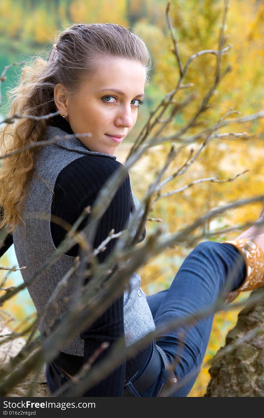 Young adult girl i in autumnal park; branches on front is not in focus. Young adult girl i in autumnal park; branches on front is not in focus