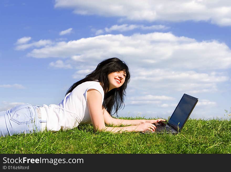 Pretty woman with laptop on the green grass