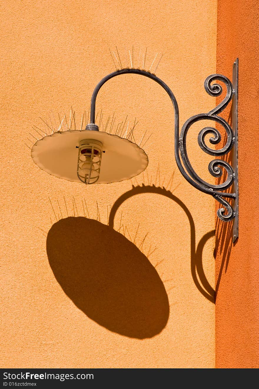 Ornate light fixture with bird-proofing spikes on a stucco wall. Ornate light fixture with bird-proofing spikes on a stucco wall.