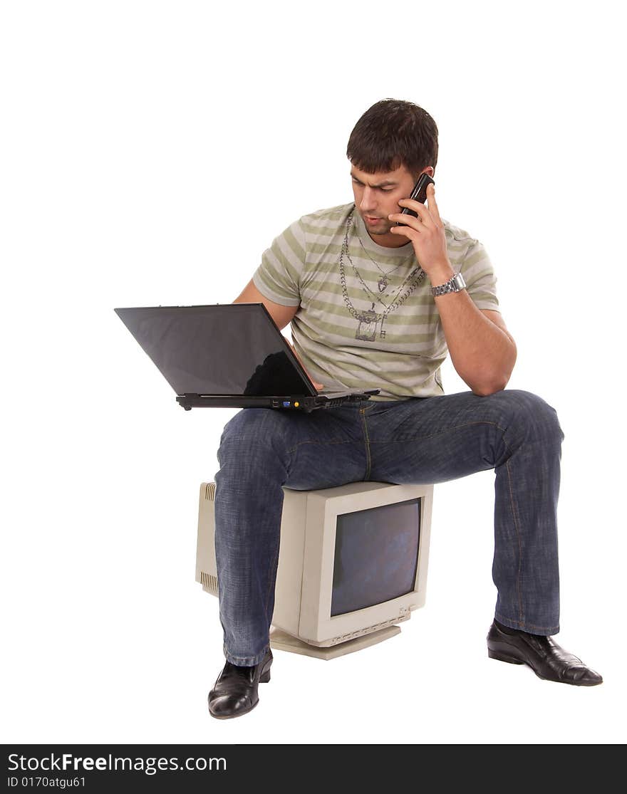 Contemporary young guy sitting on an old-fashioned computer, working with laptop and talking over a mobile phone, isolated on white background. Contemporary young guy sitting on an old-fashioned computer, working with laptop and talking over a mobile phone, isolated on white background