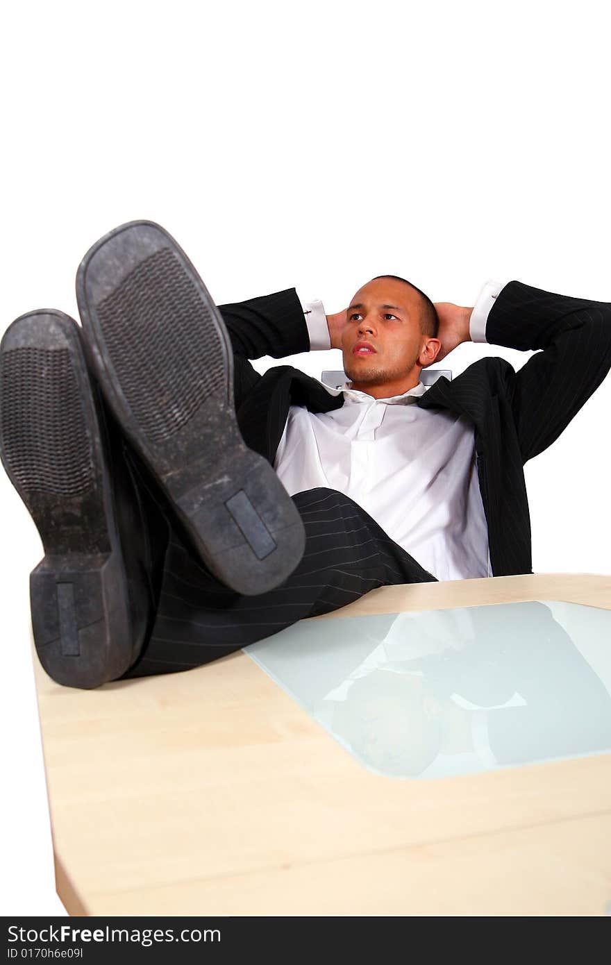 A young satisfied businessman sitting by desk at office feet on table thinking. Isolated over white. A young satisfied businessman sitting by desk at office feet on table thinking. Isolated over white.