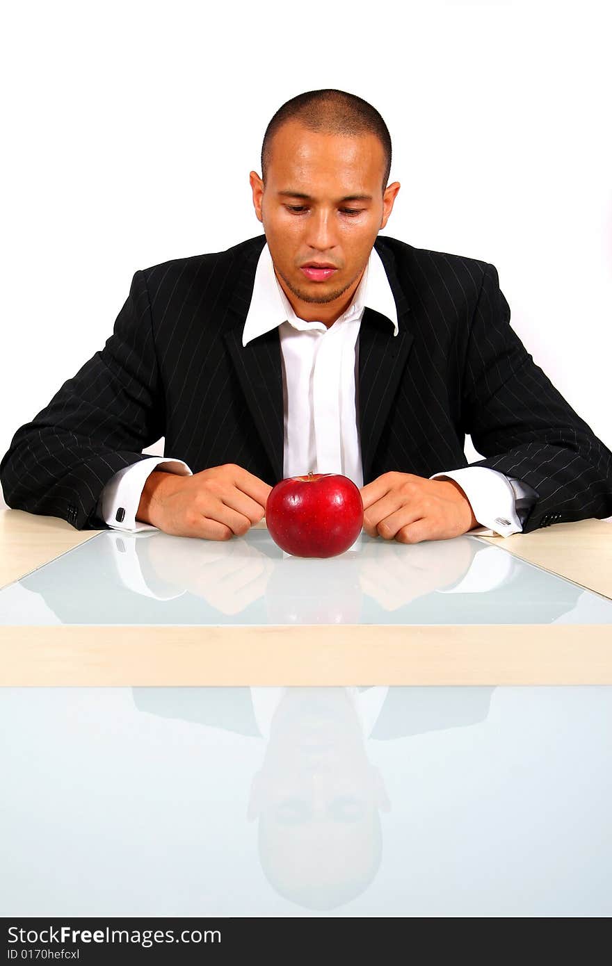 Young businessman sitting in front of a red apple thinking. Isolate over white. The table mirrors the image creating a nice effect!. Young businessman sitting in front of a red apple thinking. Isolate over white. The table mirrors the image creating a nice effect!