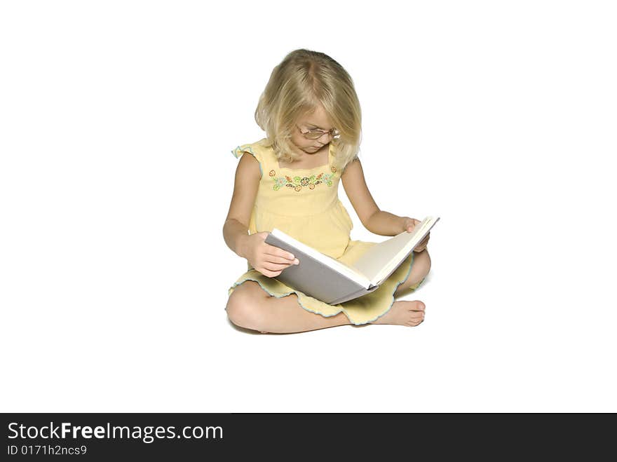 A young blonde girl sitting crosslegged while reading a textbook. Isolated on a white background. A young blonde girl sitting crosslegged while reading a textbook. Isolated on a white background