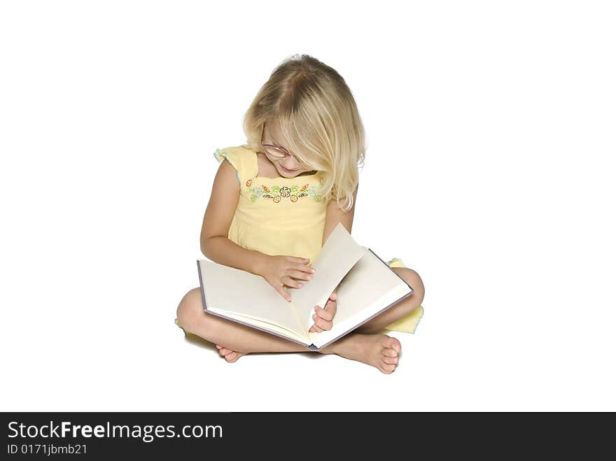 A young blonde girl sitting crosslegged while reading a textbook. Isolated on a white background. A young blonde girl sitting crosslegged while reading a textbook. Isolated on a white background