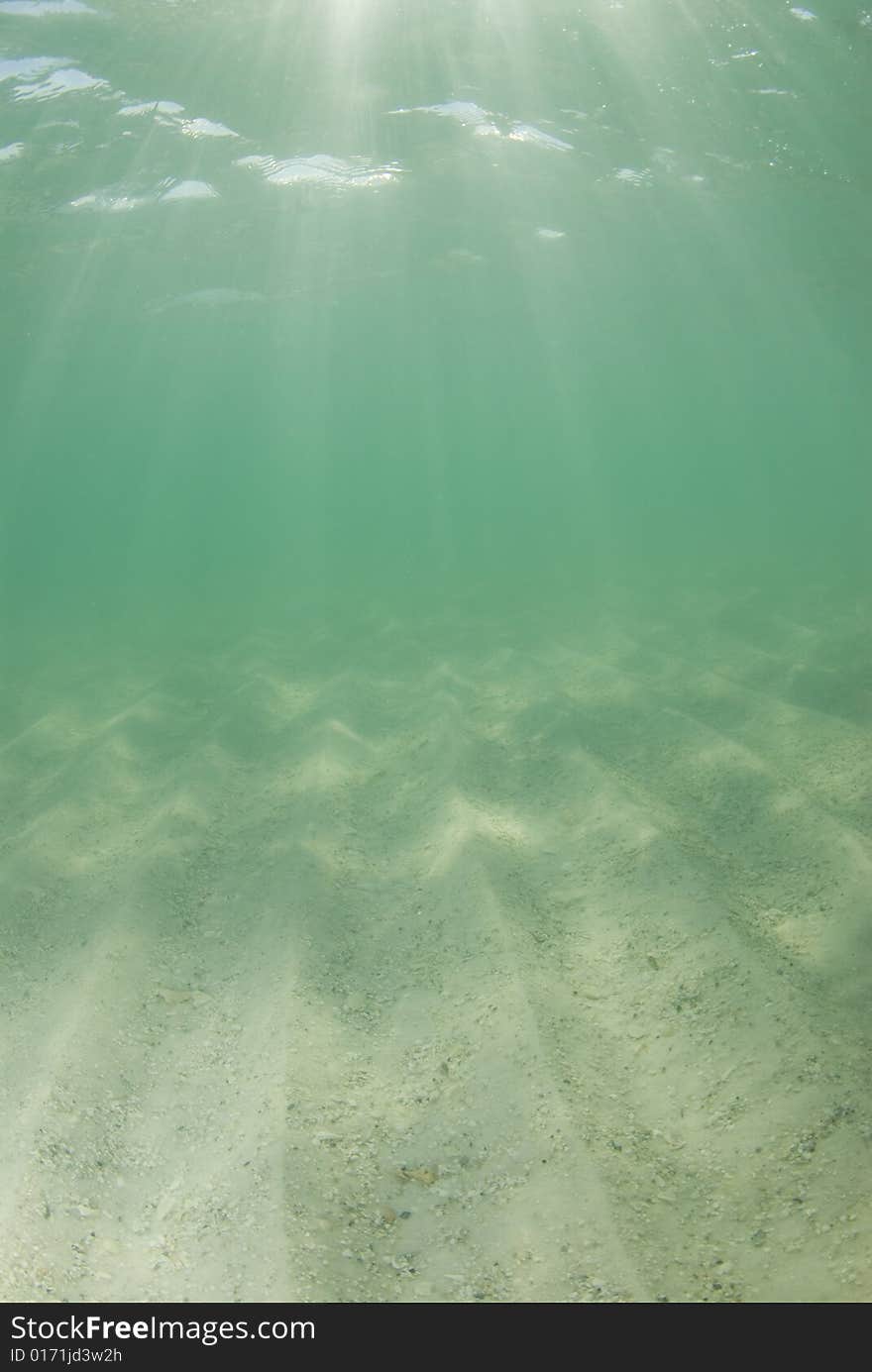 Underwater view of sunbeams stream through the surface of the ocean and dancing on the floor of the sea on a bright sunny day with dramatic sunrays. Underwater view of sunbeams stream through the surface of the ocean and dancing on the floor of the sea on a bright sunny day with dramatic sunrays.