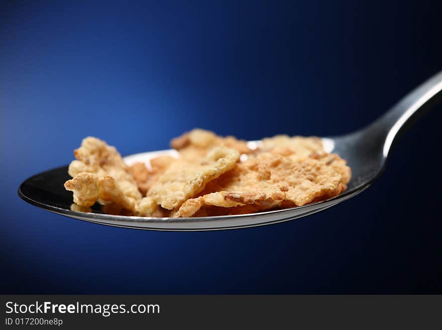 Spoon with cornflakes on blue background. Spoon with cornflakes on blue background