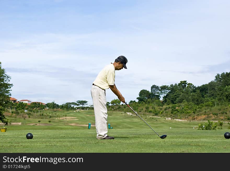 A Chinese pensioner driving off the blue tee box. A Chinese pensioner driving off the blue tee box