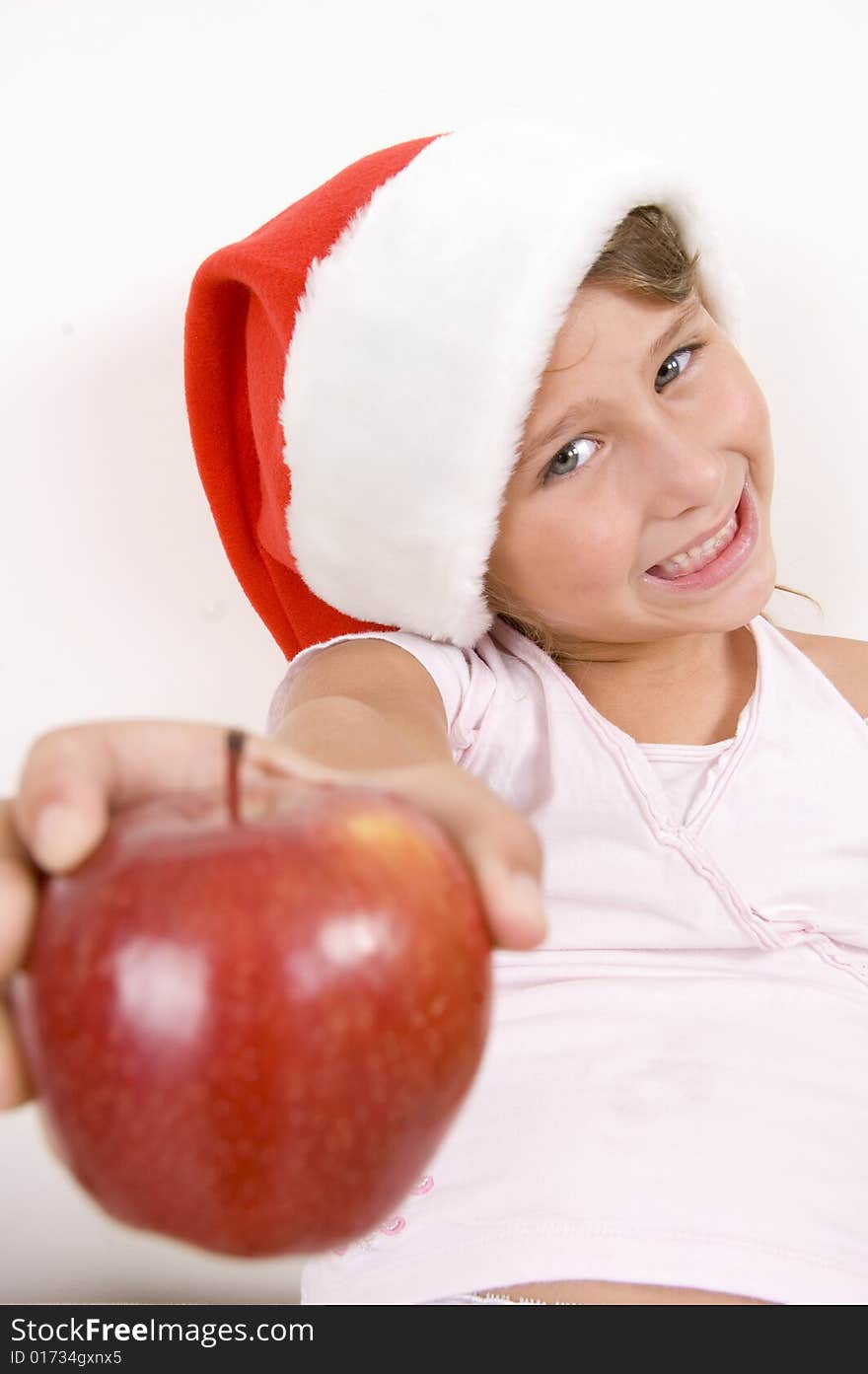 Smiling little girl with Christmas hat showing apple. Smiling little girl with Christmas hat showing apple