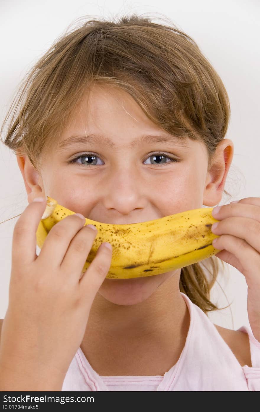 Little girl eating banana and looking at the camera
