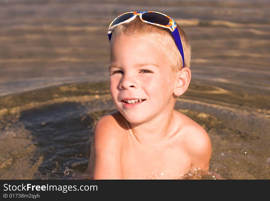 Young boy wearing sunglasses on the top of his head, sitting in the water. Young boy wearing sunglasses on the top of his head, sitting in the water.