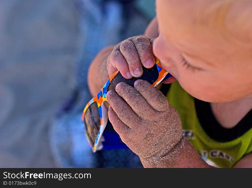 Young boy eating sunglasses full of sand. Young boy eating sunglasses full of sand