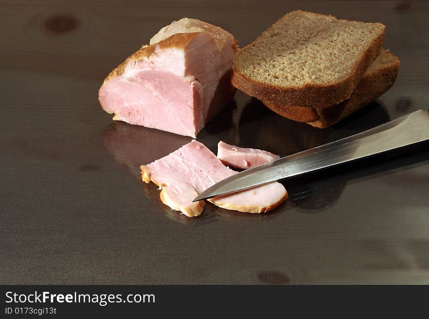 Slit ham and rye bread with kitchen knife on glassy table. Slit ham and rye bread with kitchen knife on glassy table