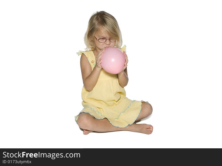 A young girl in a yellow dress sitting down and blowing up a pink balloon.  Isolated on a white background. A young girl in a yellow dress sitting down and blowing up a pink balloon.  Isolated on a white background