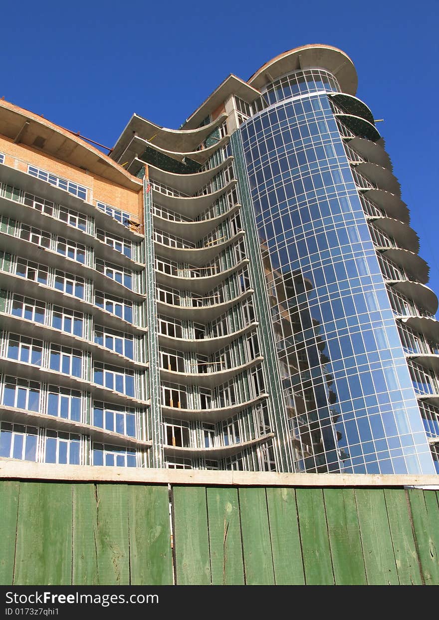 The Construction of the building. The Sun sparkles in new glass, on background blue sky.