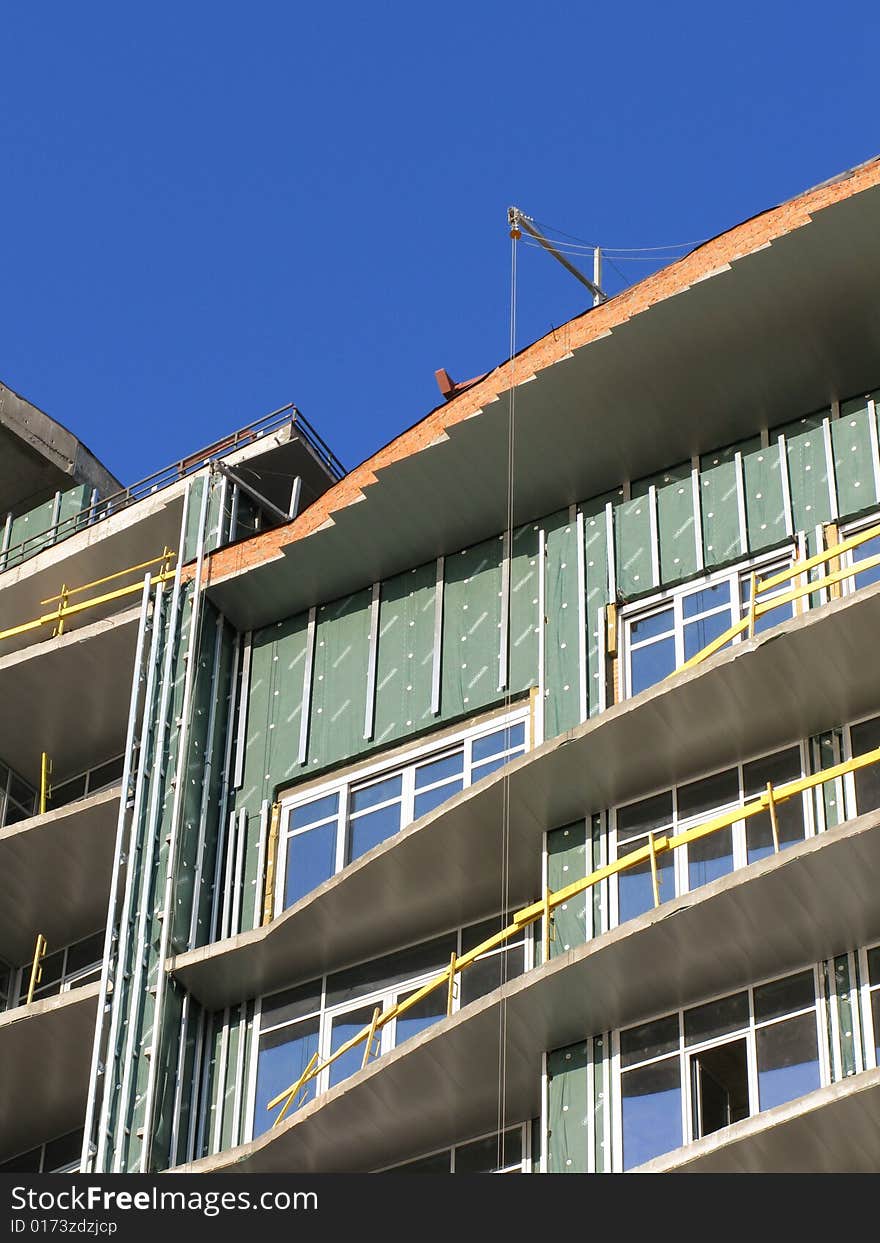 The Construction of the building. The Sun sparkles in new glass, on background blue sky.