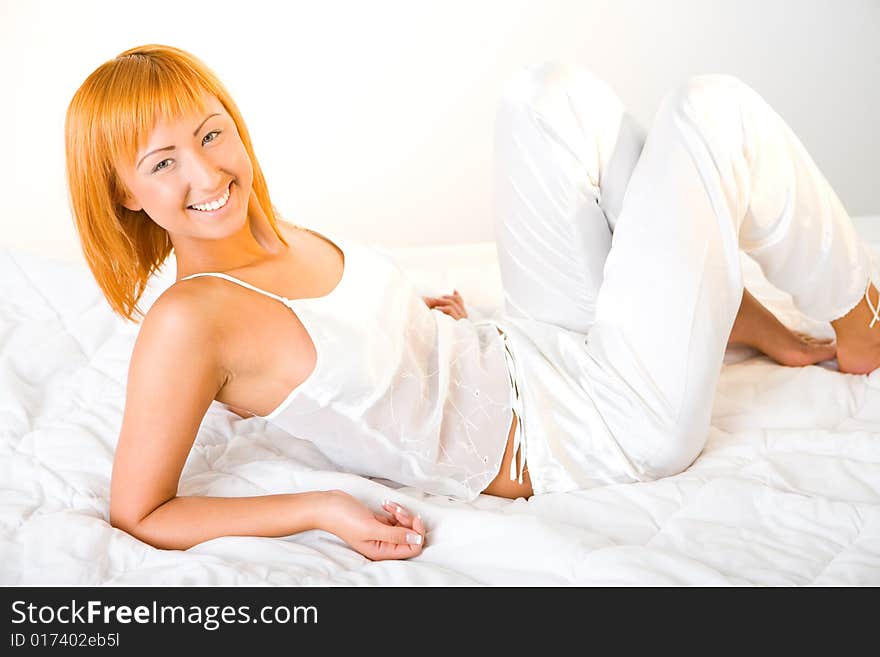 Young red-haired woman lying in bed. She's smiling and looking at camera. Side view. Young red-haired woman lying in bed. She's smiling and looking at camera. Side view.