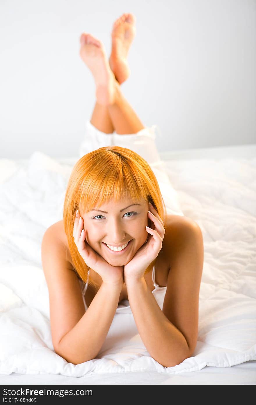 Young red-haired woman lying in bed. She's smiling and looking at camera. High angle view. Young red-haired woman lying in bed. She's smiling and looking at camera. High angle view.