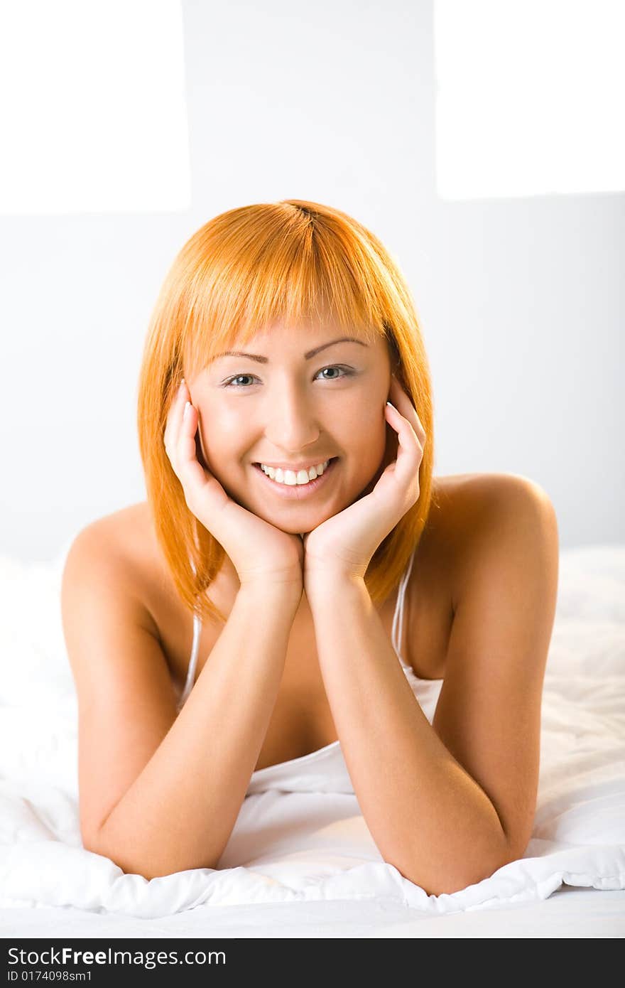 Young red-haired woman lying in bed. She's smiling and looking at camera. Front view. Closeup on face. Young red-haired woman lying in bed. She's smiling and looking at camera. Front view. Closeup on face.