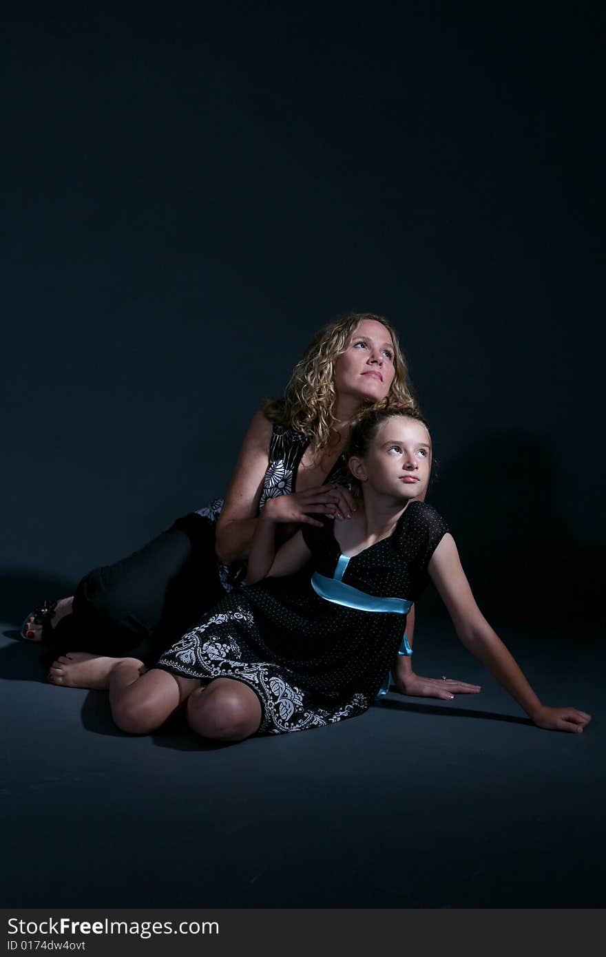 Mother and daughter on the floor together on a dark background. Mother and daughter on the floor together on a dark background