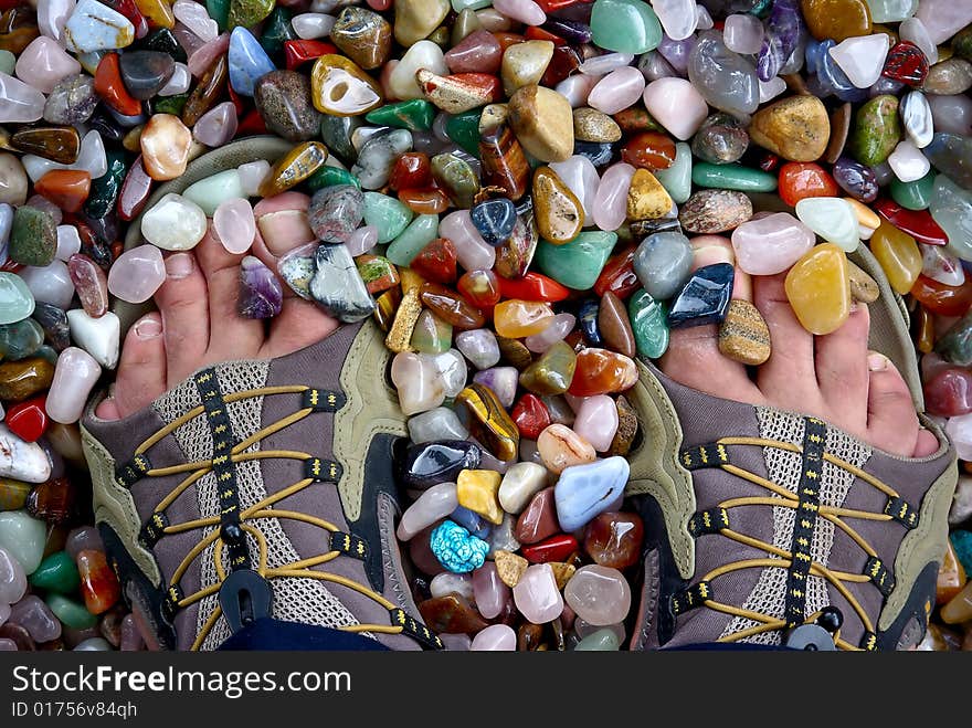 Feet at sandal footwear standing on coloured grinded semiprecious background. Feet at sandal footwear standing on coloured grinded semiprecious background