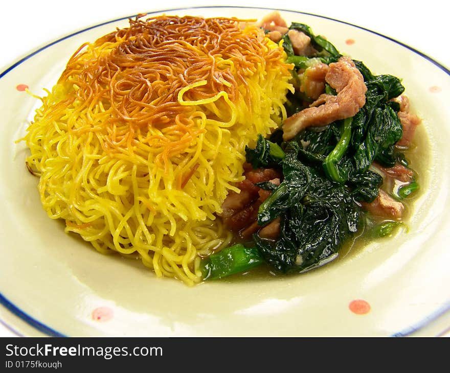 Closeup of a dish of Chinese fried noodles with green vegetable and ham on a ceramic plate. Closeup of a dish of Chinese fried noodles with green vegetable and ham on a ceramic plate