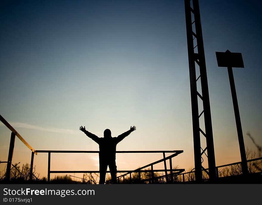 The man standing next to the bridge rising his hands to the colorful sky. The man standing next to the bridge rising his hands to the colorful sky