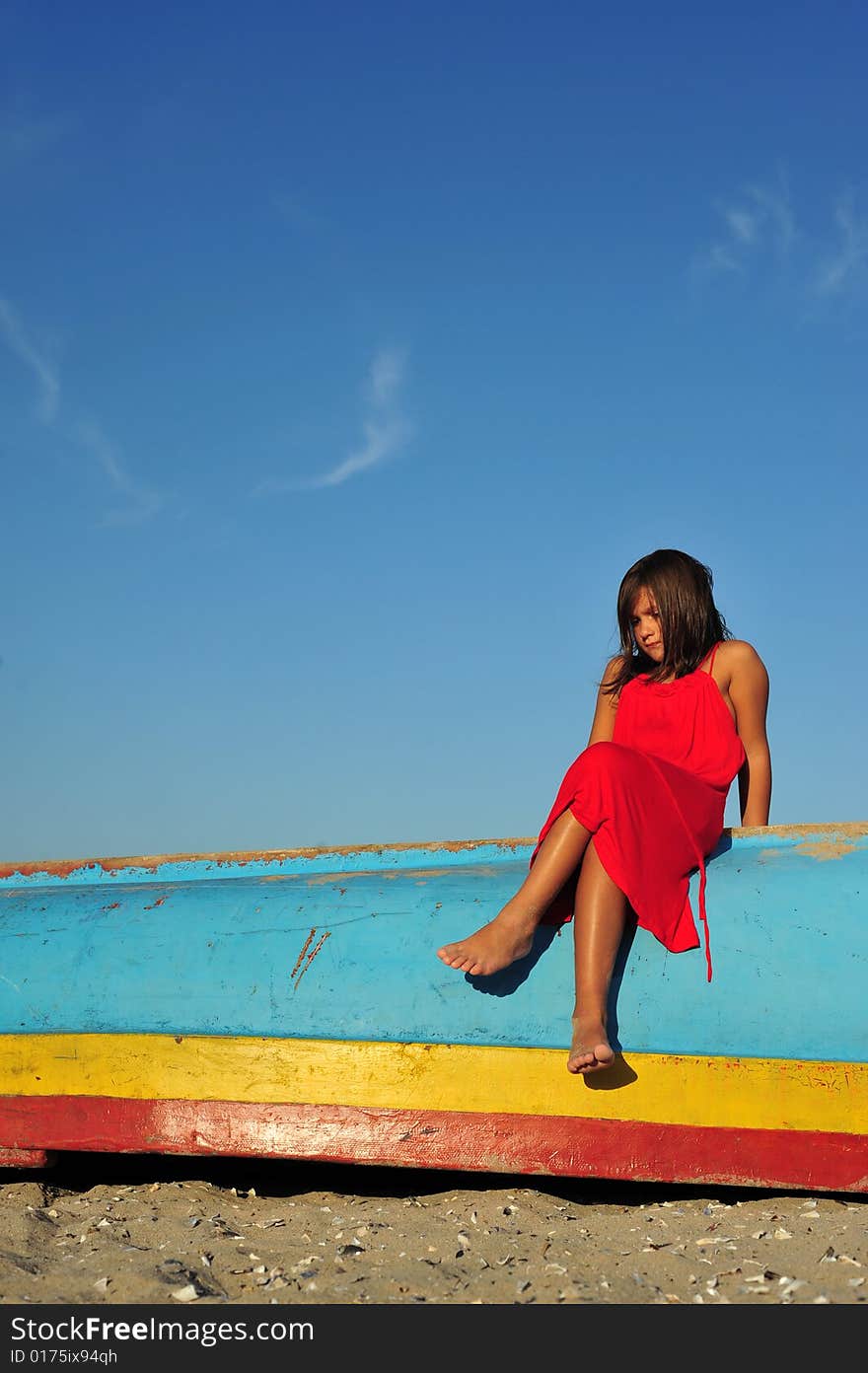 Young girl in red dress standing on boat on beach