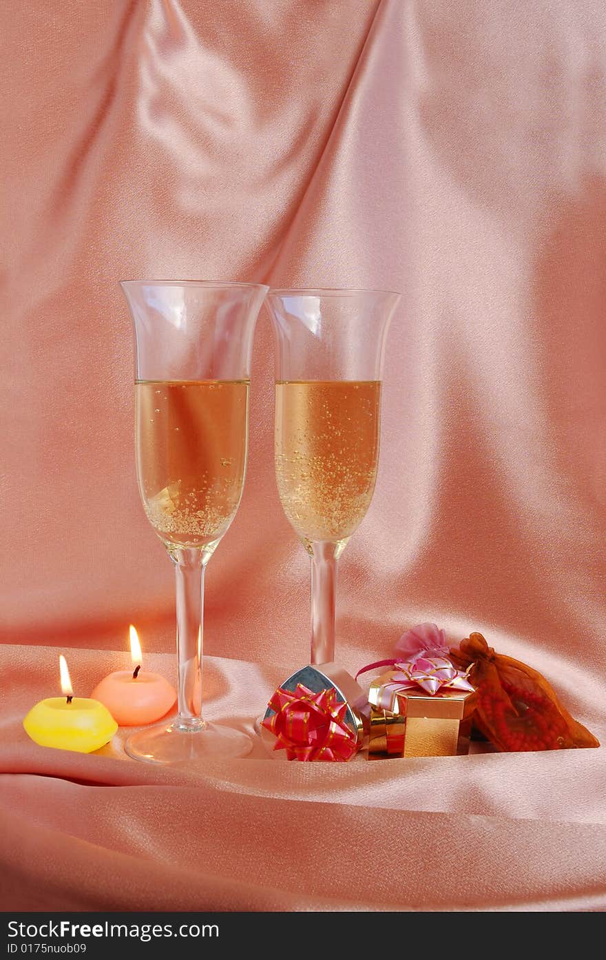 Pair of champagne flutes with candles and gift box on silk background