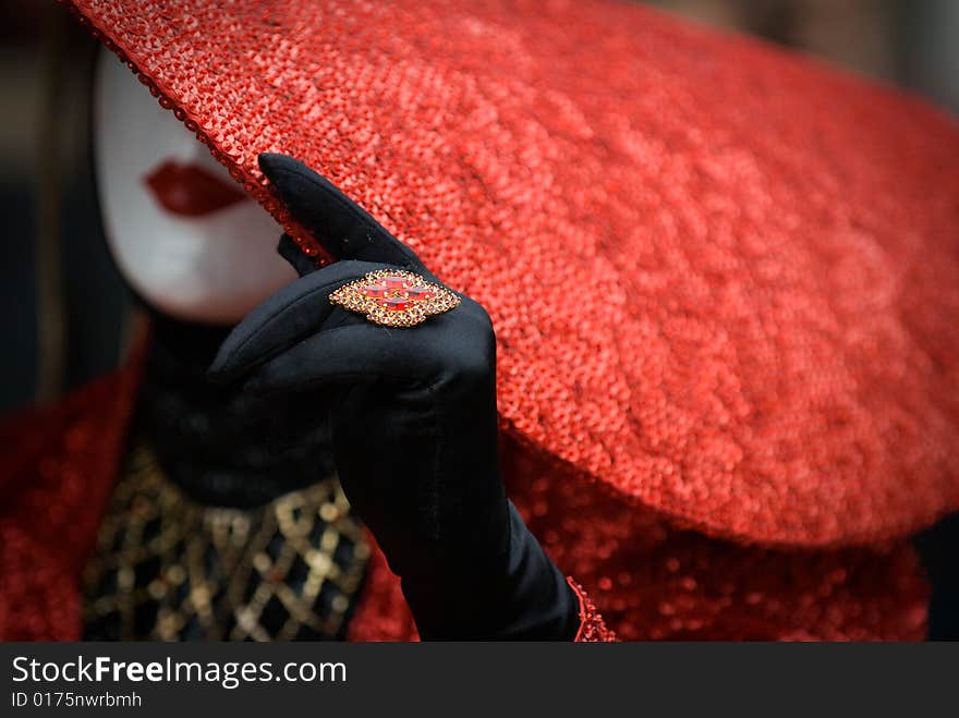 Person wearing a white mask with red hat , black gloves and ring at the Venezzia carvival. Person wearing a white mask with red hat , black gloves and ring at the Venezzia carvival