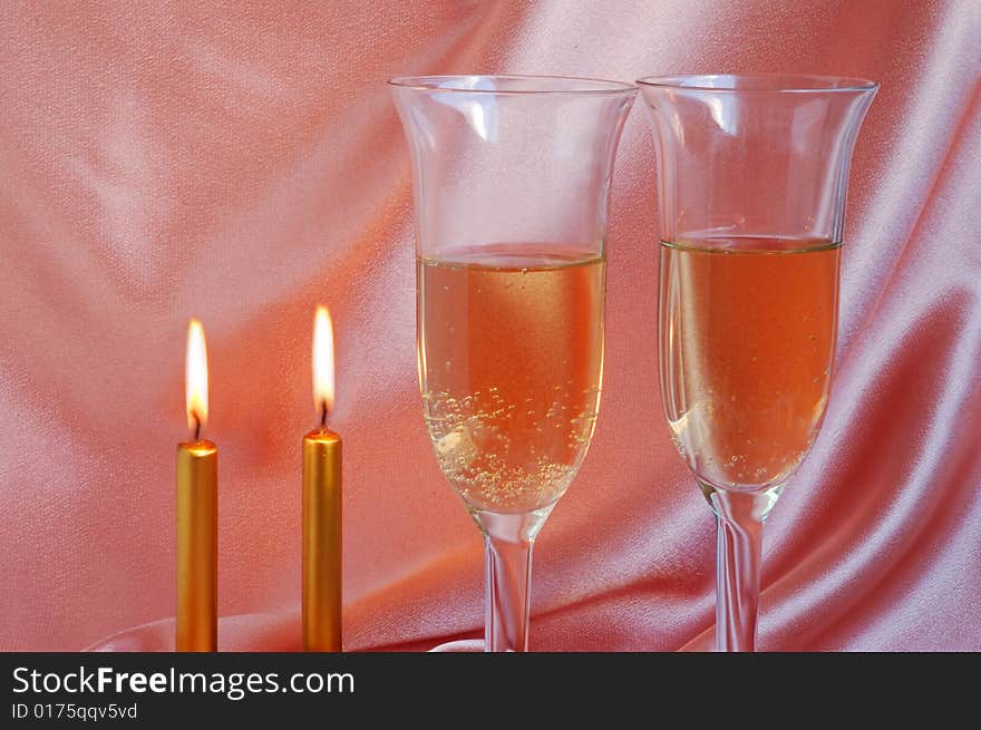 Pair of champagne flutes with candles on silk background