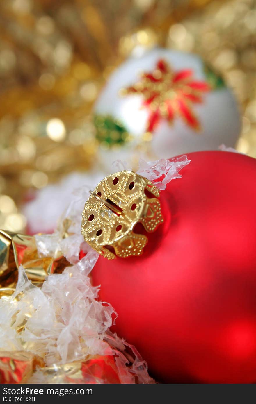 Close up with selective focus of a red Christmas ornament, along with fake snow and gold metallic background.