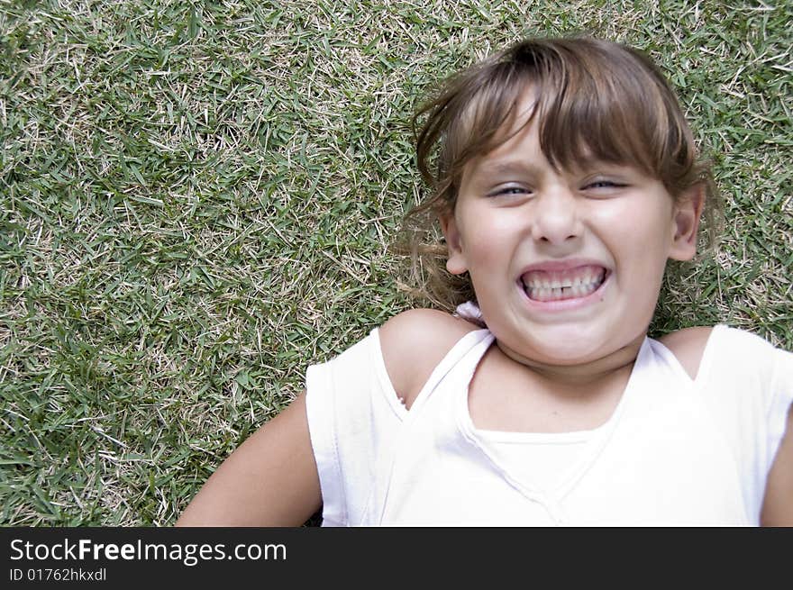 Girl laying down on grass with clenched teeth. Girl laying down on grass with clenched teeth