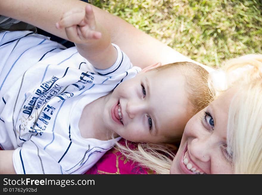 Blonder young mother posing with her baby lying on grass. Blonder young mother posing with her baby lying on grass