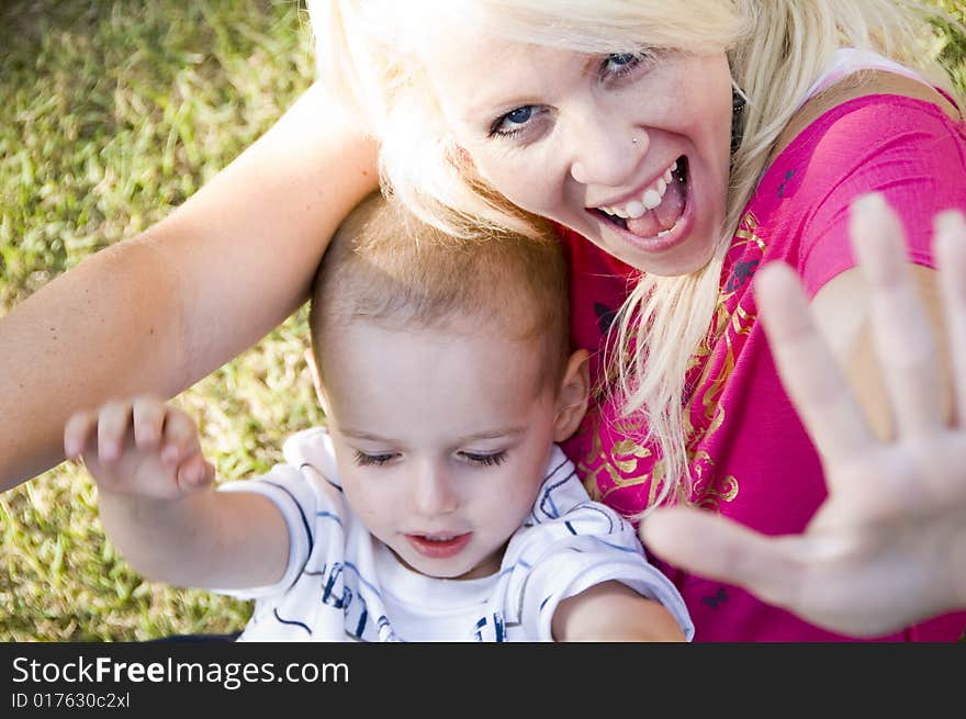 Cheerful young woman and little baby sitting on green grass