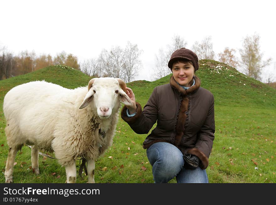 The girl poses with white sheep on lawn. The girl poses with white sheep on lawn