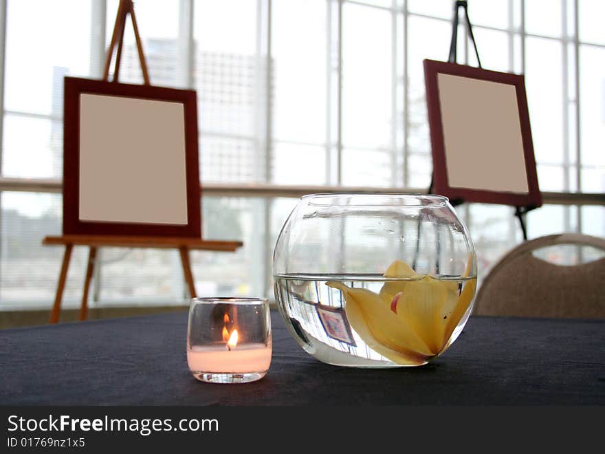 Two blank canvases sit in the background with a candle and floating flower in the foreground. Two blank canvases sit in the background with a candle and floating flower in the foreground.