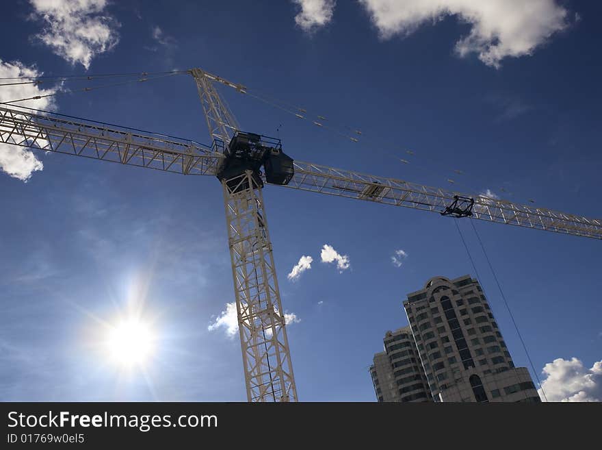 Low angle shot of a construction crane in the city against a blue sky with framed by white clouds, with a dramatic lens flare. Low angle shot of a construction crane in the city against a blue sky with framed by white clouds, with a dramatic lens flare.