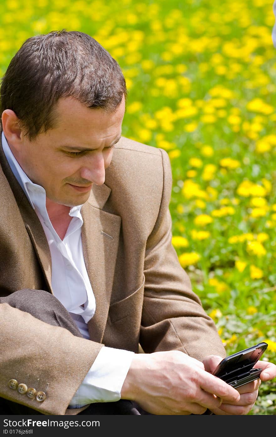 Businessman with mobile technology in a meadow with dandelions. Businessman with mobile technology in a meadow with dandelions