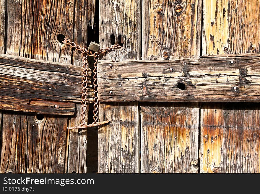 Old wooden door secured with a padlock and iron chain