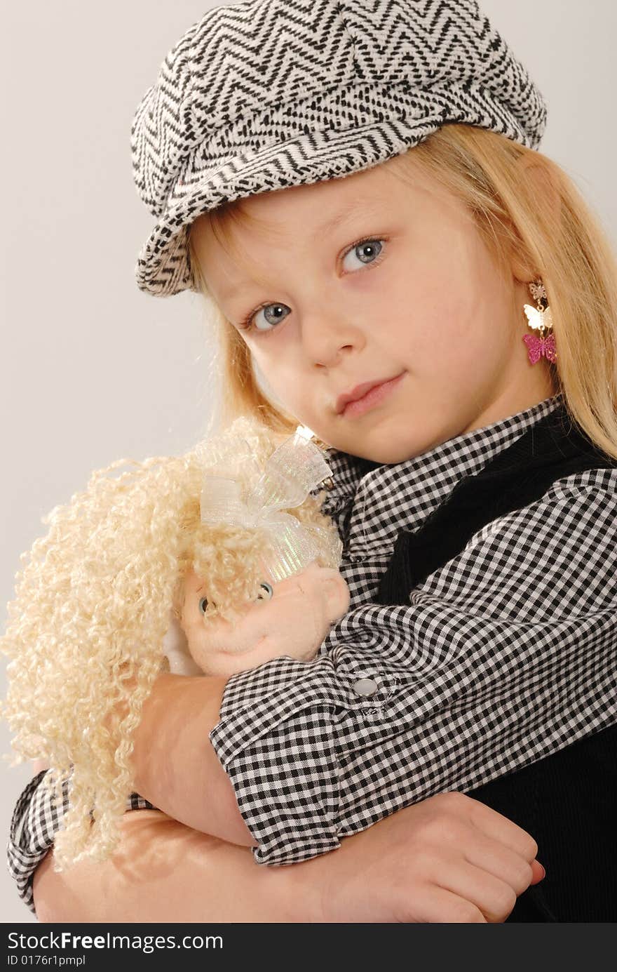 Cute blonde girl in checked cap cuddles doll. Cute blonde girl in checked cap cuddles doll