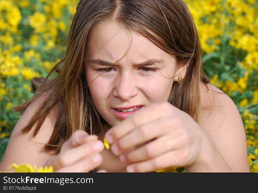 Girl lying on stomach in flower field looking at petal in summer. Girl lying on stomach in flower field looking at petal in summer