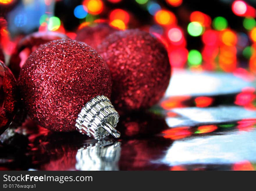 A red Christmas ornament on a reflective background with blurred lights to the far back. Copy space available. A red Christmas ornament on a reflective background with blurred lights to the far back. Copy space available.