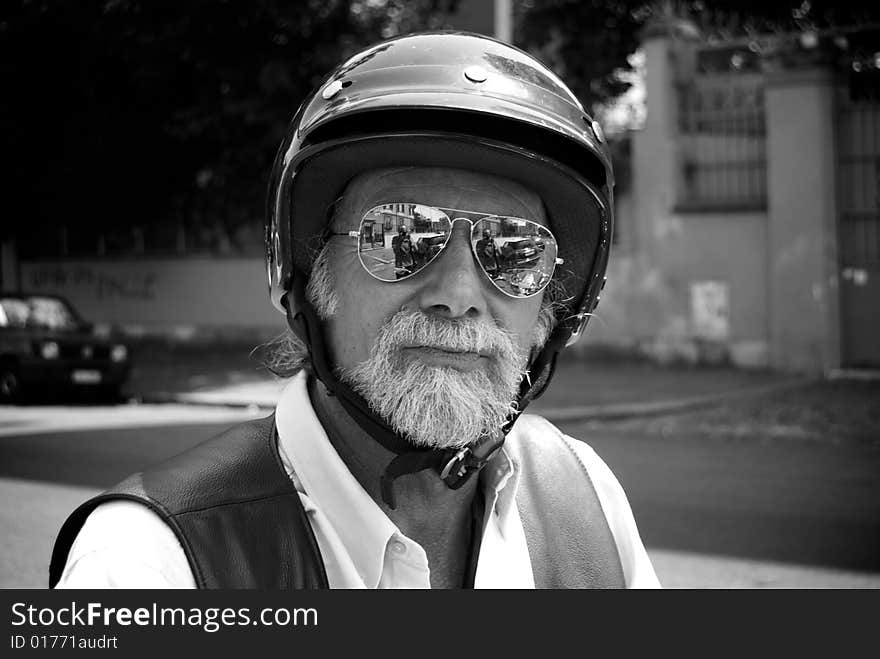 In this shot there is an old man who is riding his motorbike. he wears sun glasses and he has a long beard. In this shot there is an old man who is riding his motorbike. he wears sun glasses and he has a long beard.