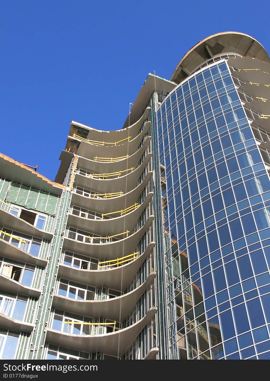 The Construction of the building. The Sun sparkles in new glass, on background blue sky.