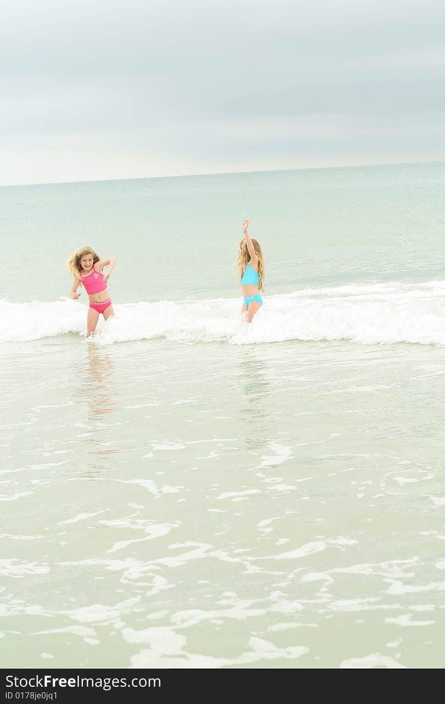 Twin sisters running from the waves vertical